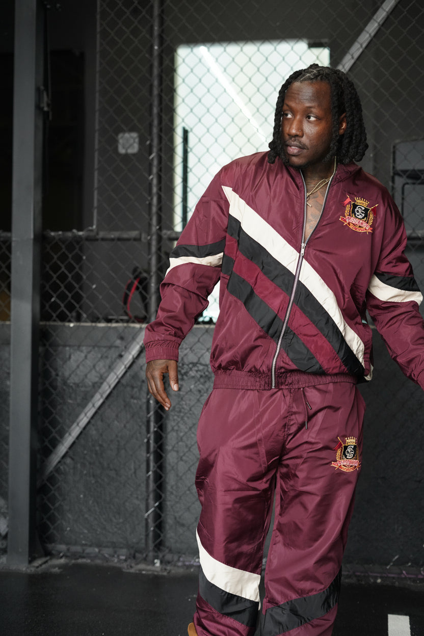 Man wearing a maroon tracksuit with black and white stripes in an urban setting